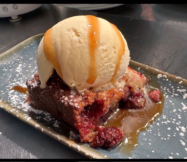 Brownie with berry filling, vanilla ice cream, and caramel sauce on a blue rectangular plate.