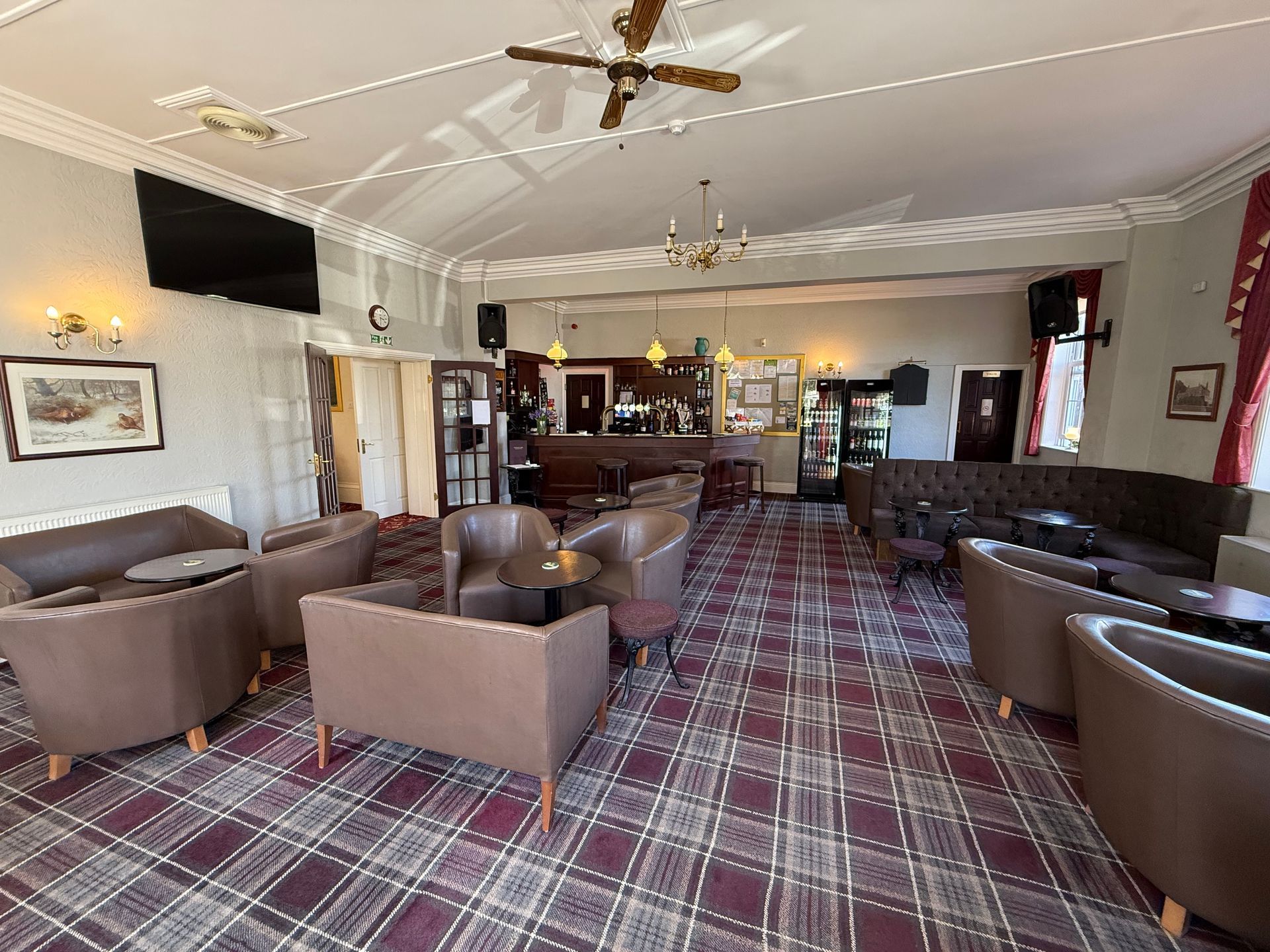 A spacious lounge area with a bar, brown seating, and a plaid carpet.