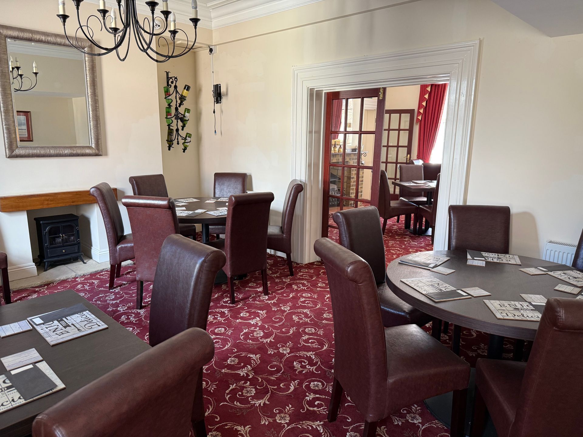A room with round tables, chairs, and a fireplace. A chandelier hangs from the ceiling.