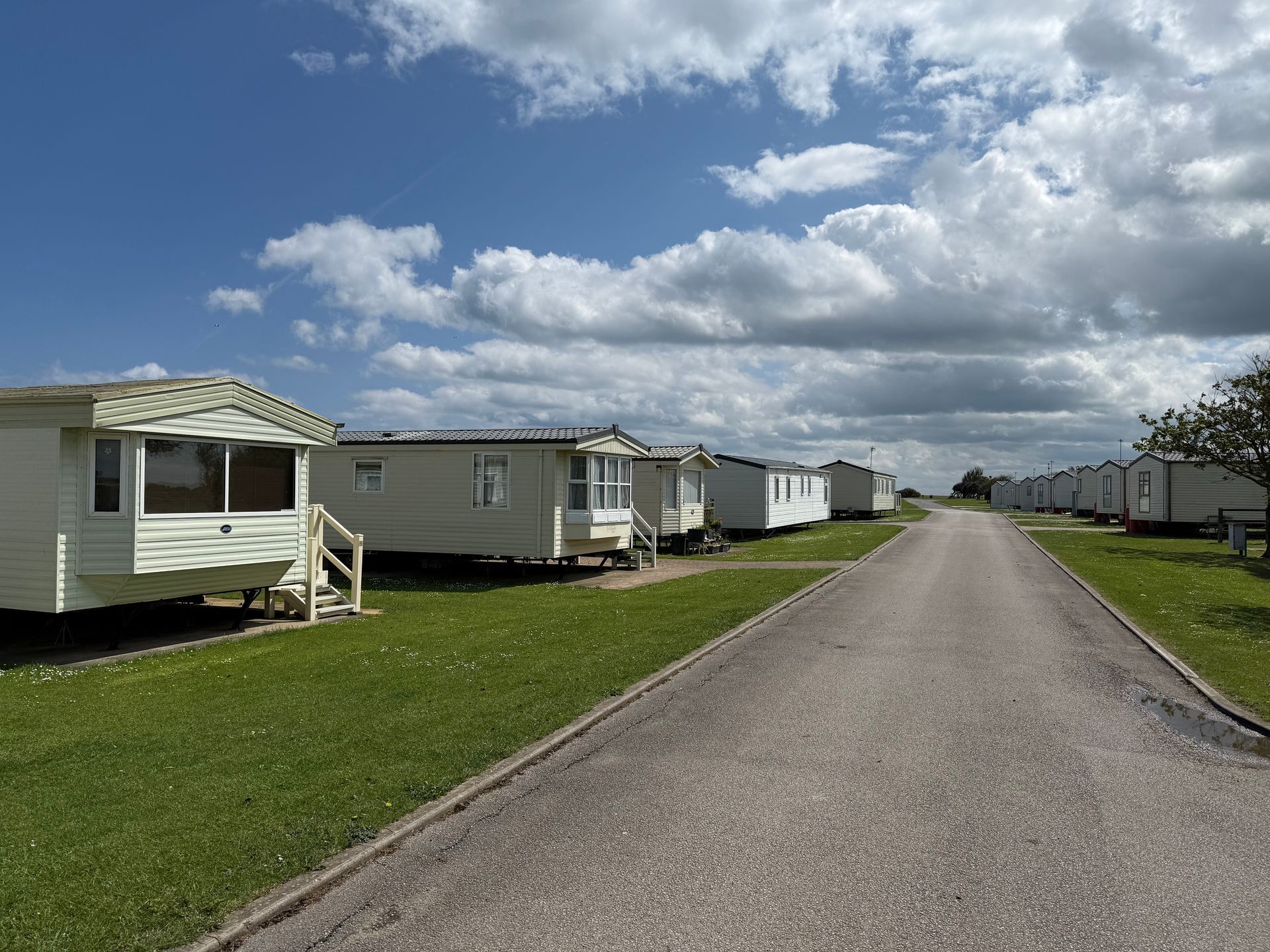 Row of white caravans on a grassy area, gray road, blue sky with clouds.