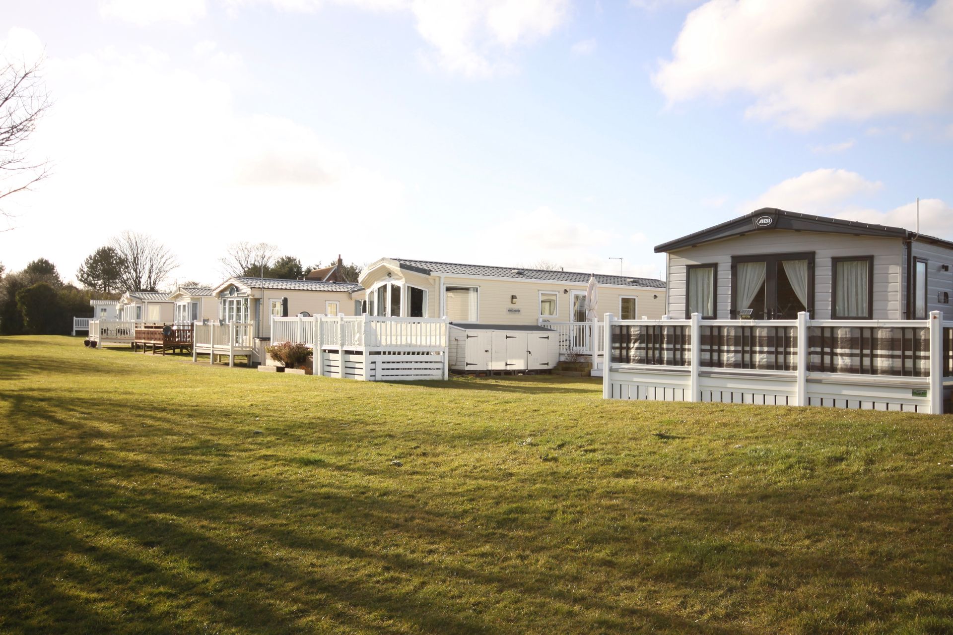 Row of white caravans on a green grassy field in a sunny setting.