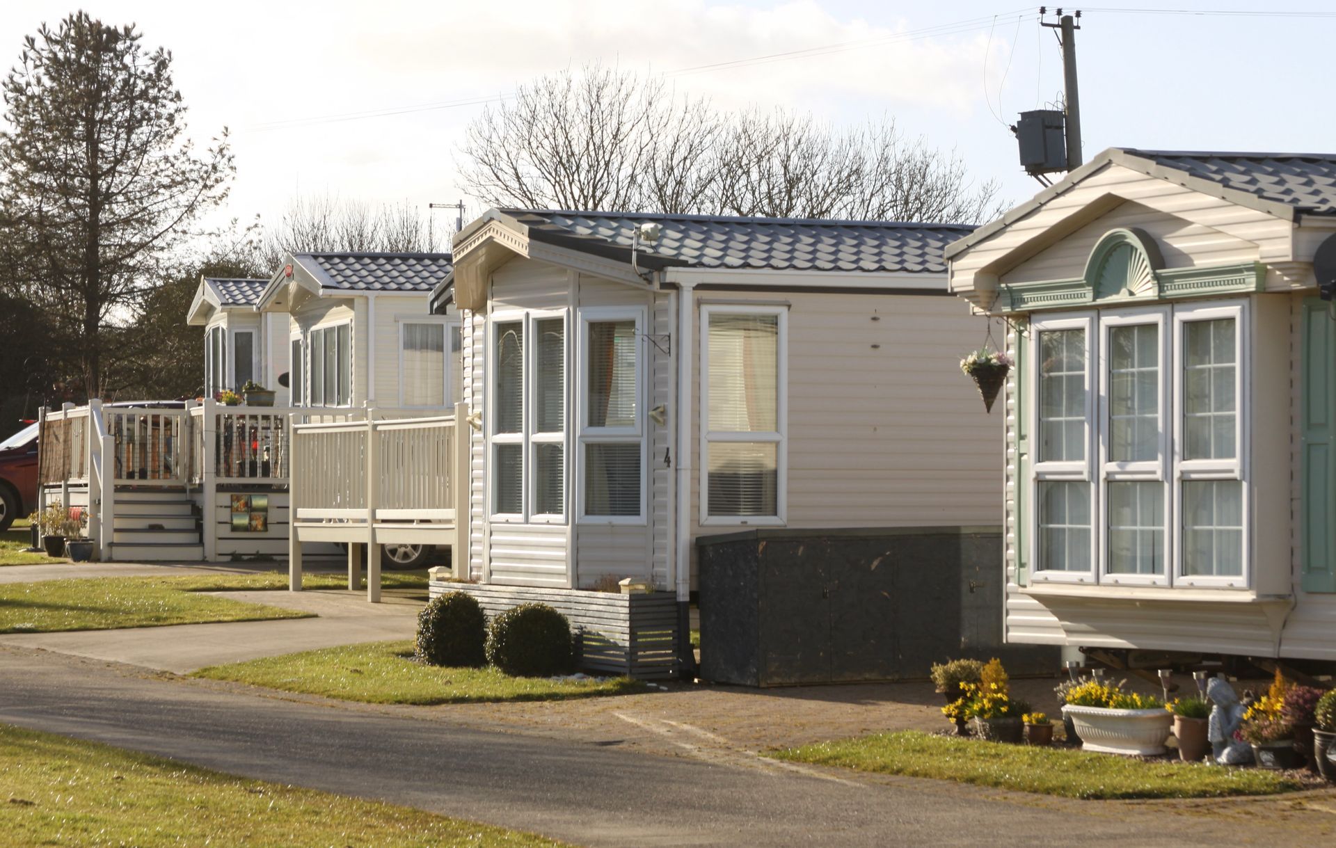 Mobile homes in a row, with light-colored siding, windows, and small yards, set on a grassy area.