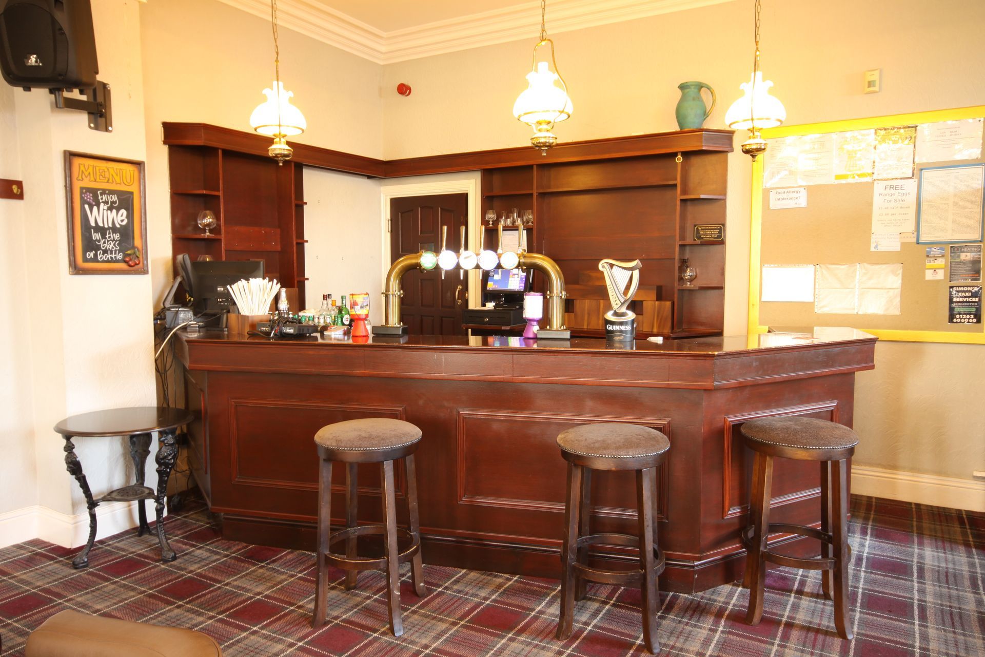 Bar with wooden counter, stools, beer taps, and display shelves. A notice board is on the right.