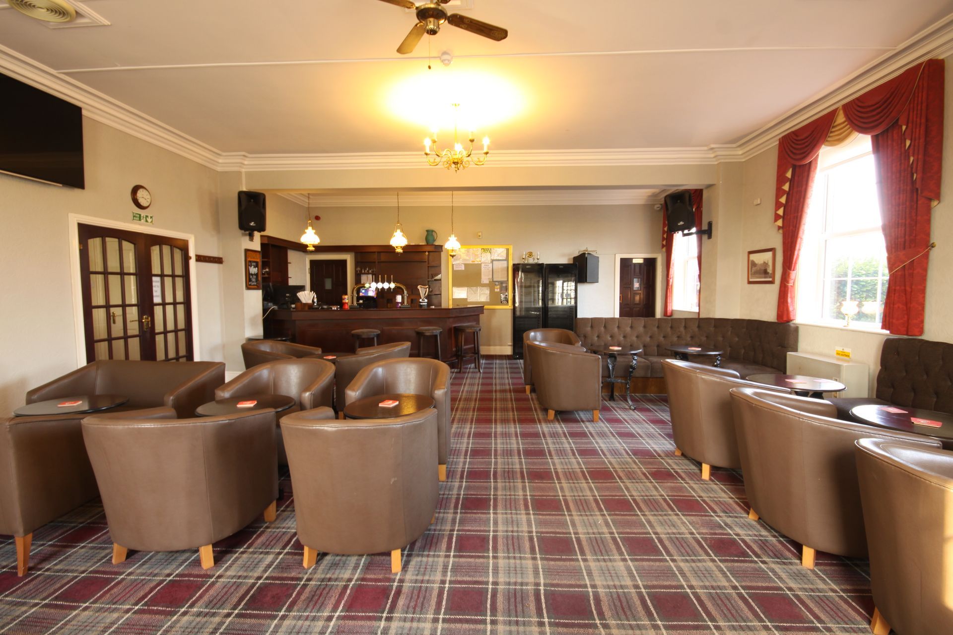 Brown leather armchairs and couches in a bar with a checkered carpet and a wooden bar in the background.