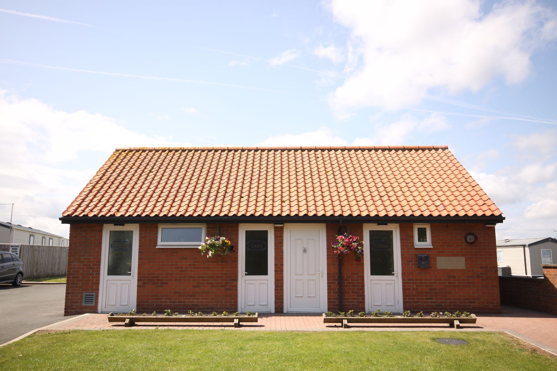 Red brick building with terracotta tile roof, white doors, and flower boxes, on a sunny day.