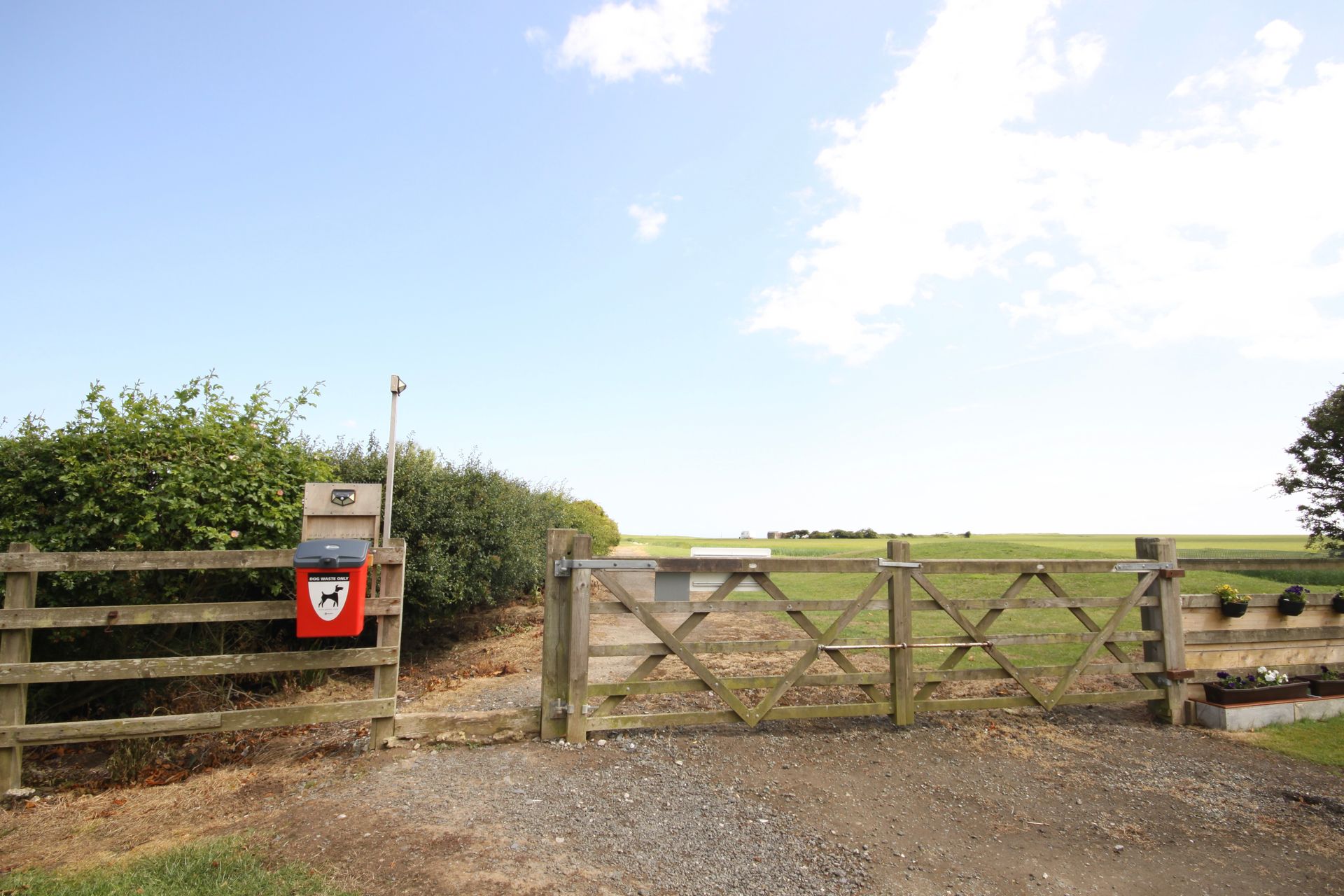 Wooden gate and mailbox with a red emblem, leading to a field under a blue sky.