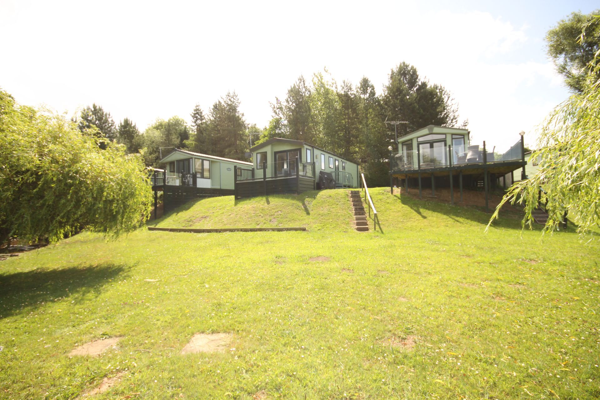 Green grassy hill with several holiday caravans, trees and a sunny sky.