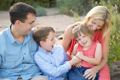 Family sitting outdoors, smiling and playing together on a blanket in soft sunlight