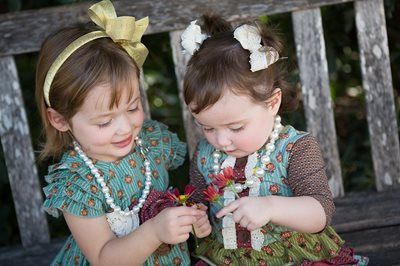 Two children on a bench sharing flowers, one in a yellow bow and one with a white hair bow