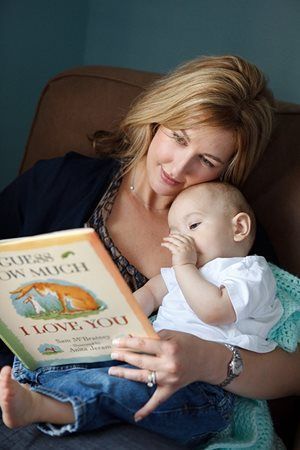Woman reading a book to a baby on her lap in a brown chair