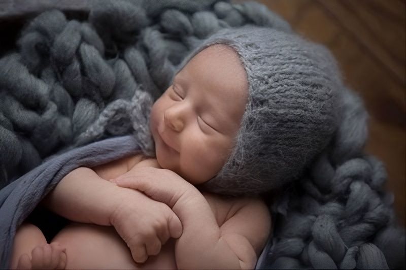 Sleeping newborn in a gray knit hat, wrapped in a soft gray blanket.