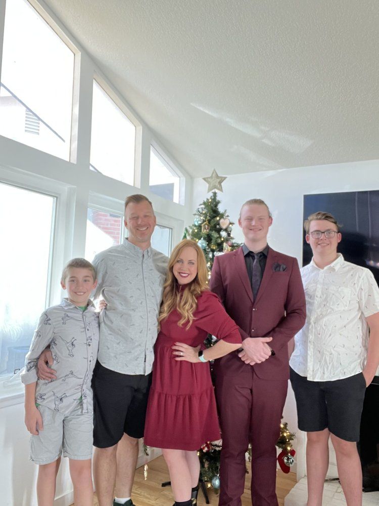 Family posing by Christmas tree. Woman in red dress, men in shirts and suit, boy in shorts. Bright room.