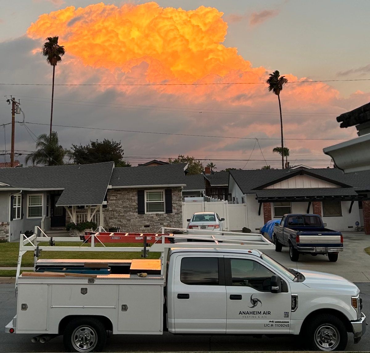 White service truck parked in residential street under orange-lit sunset sky.