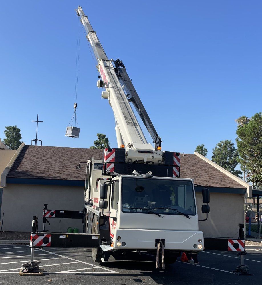 A crane lifting a square object near a building with a brown roof and a cross against a blue sky.