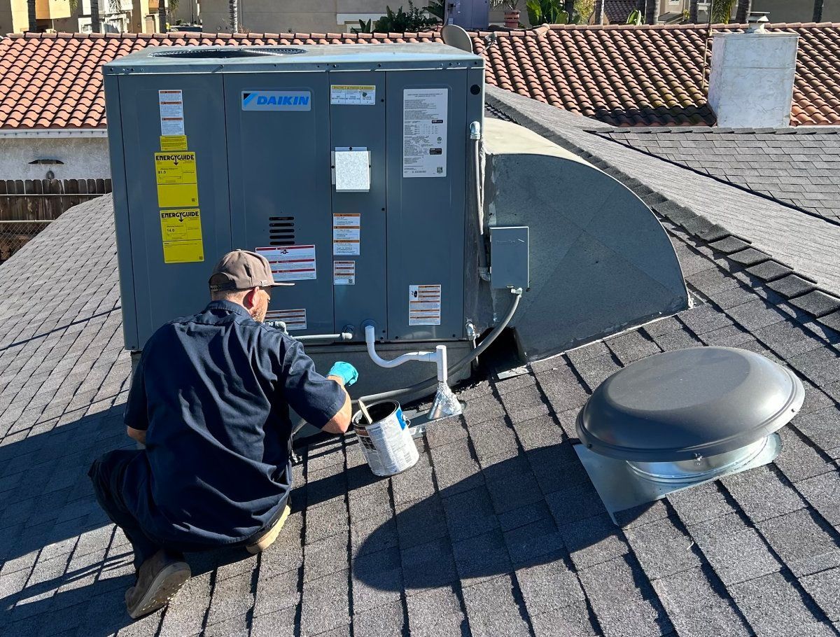 HVAC technician on a roof, inspecting an air conditioning unit. Gray unit, dark roof, sunny day.