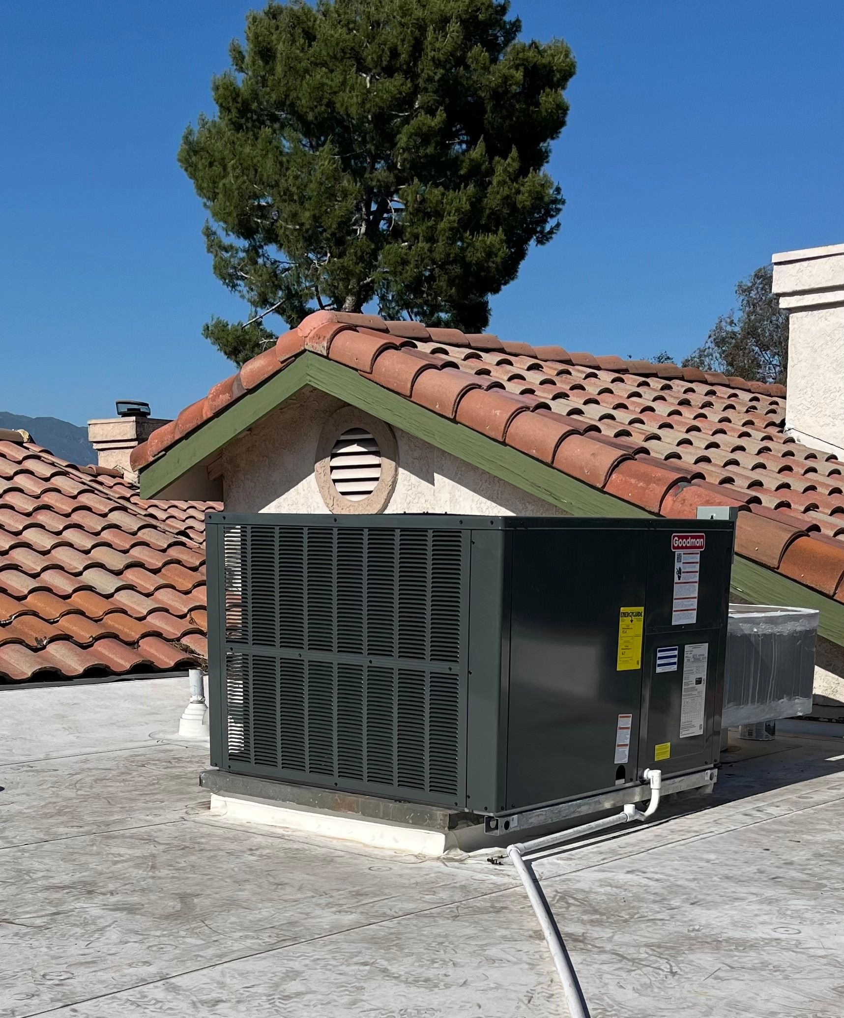 Large rooftop HVAC unit beside red tile roofs under a clear blue sky