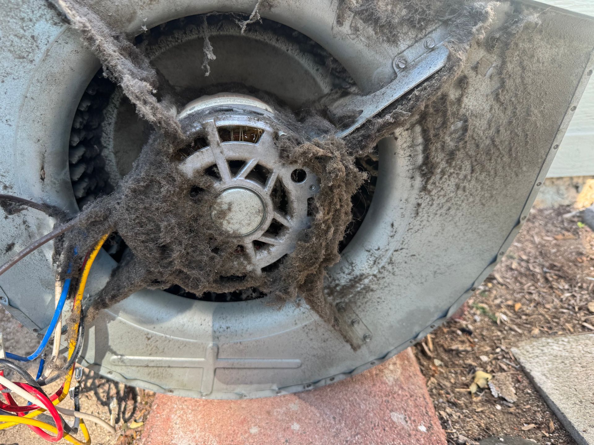 Dirty outdoor fan housing with exposed wires and dusty blades exposed inside the unit