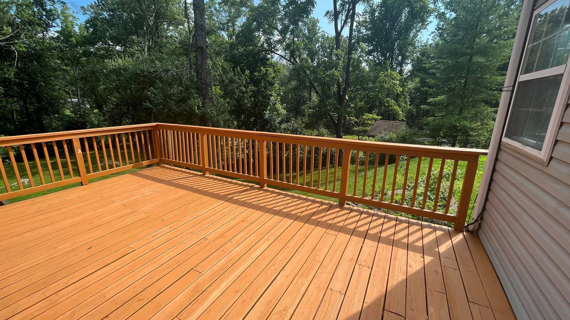 A large wooden deck with a railing and trees in the background