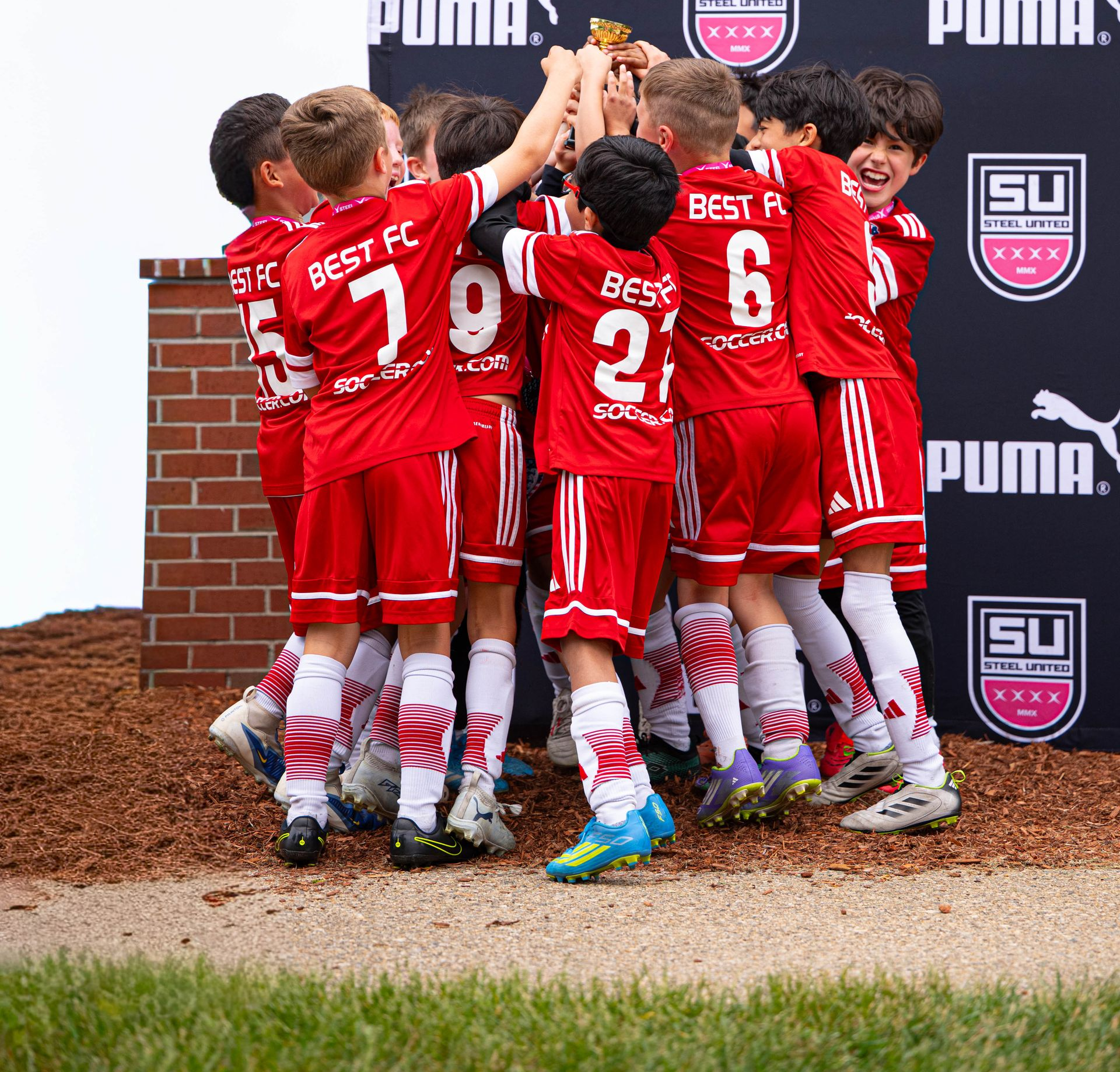 BEST FC soccer team in red uniforms huddling in celebration 