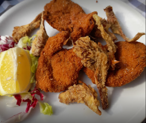 Un piatto con cotolette fritte impanate, funghi ostrica fritti dorati, uno spicchio di limone fresco e un contorno di insalata.