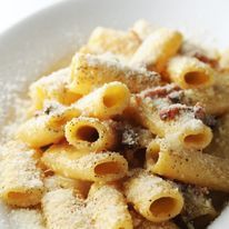 Primo piano di rigatoni conditi con una cremosa salsa allo speck, guarniti con formaggio grattugiato e pepe nero macinato.