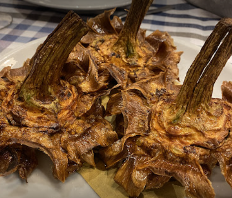 Tre carciofi fritti, dorati e croccanti, serviti su un piatto bianco con un foglio di carta da forno.