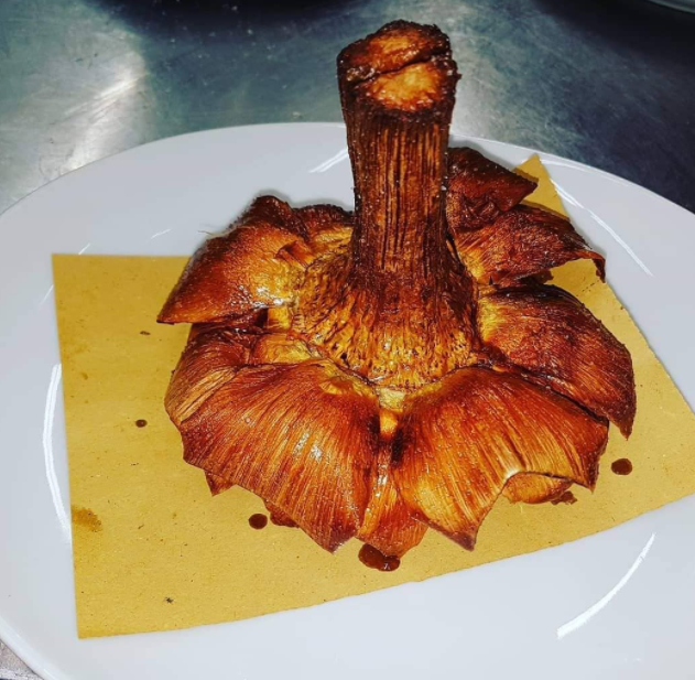 Un carciofo fritto, dorato e croccante, servito capovolto su un piatto bianco foderato con un tovagliolo giallo.