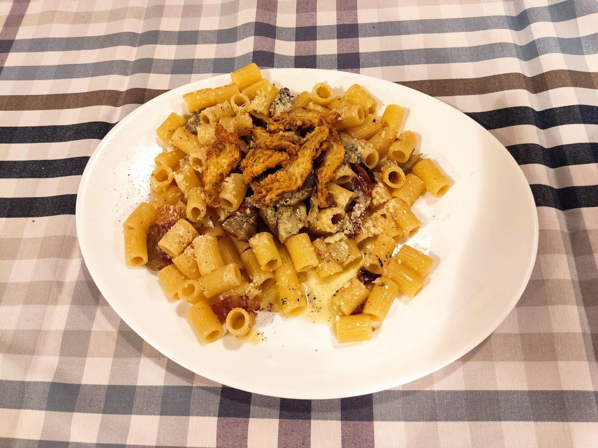 Un piatto di rigatoni con salsa cremosa e pezzi di pollo rosolati, servito su una tovaglia a quadri blu e bianchi.
