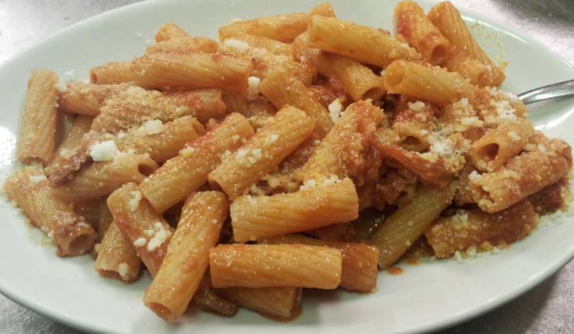 Un piatto di rigatoni conditi con una salsa di pomodoro rossastra e cosparsi di formaggio grattugiato.