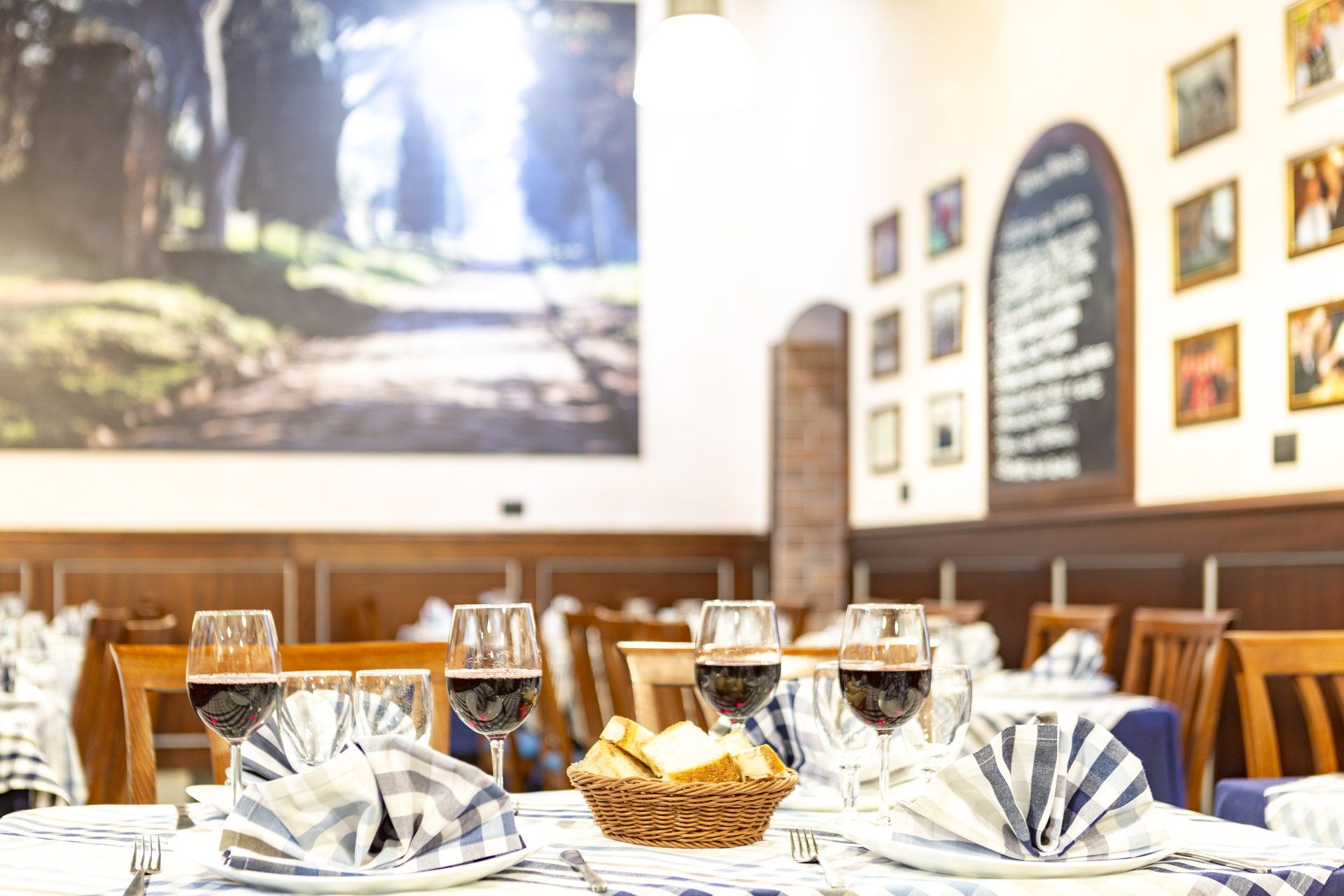 In un ristorante in stile italiano, la tavola è apparecchiata con bicchieri da vino, tovaglioli di stoffa e un cestino di pane.