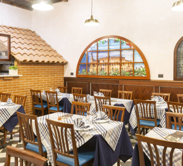 La sala da pranzo di un ristorante in stile rustico, con tovaglie a quadri, sedie in legno e un grande murale ad arco raffigurante una scena cittadina.