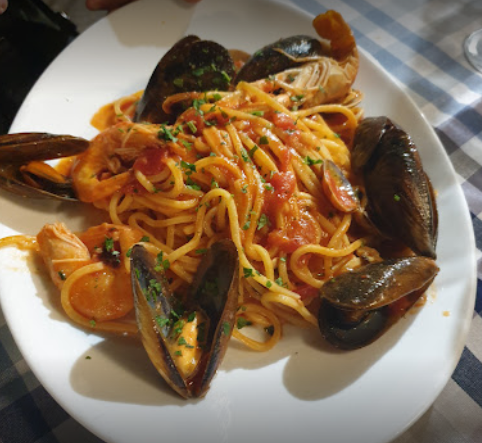 Un piatto di pasta ai frutti di mare con cozze e gamberi in salsa di pomodoro, servito su una tovaglia a quadri blu e bianchi.