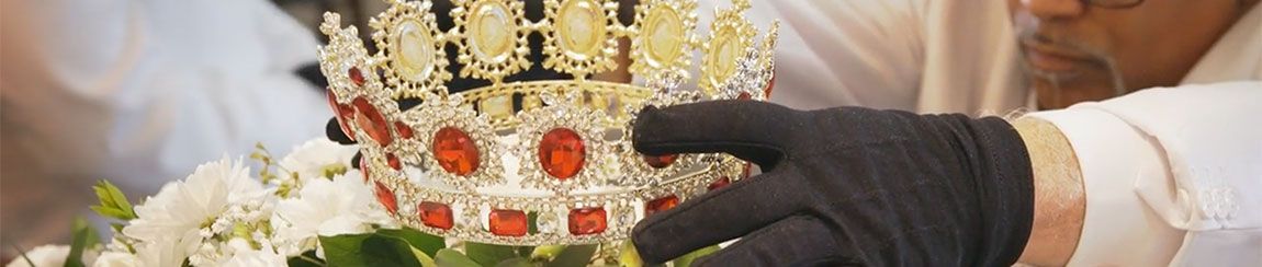 Gloved hands laying an ornate crown atop a spray of flowers and greenery