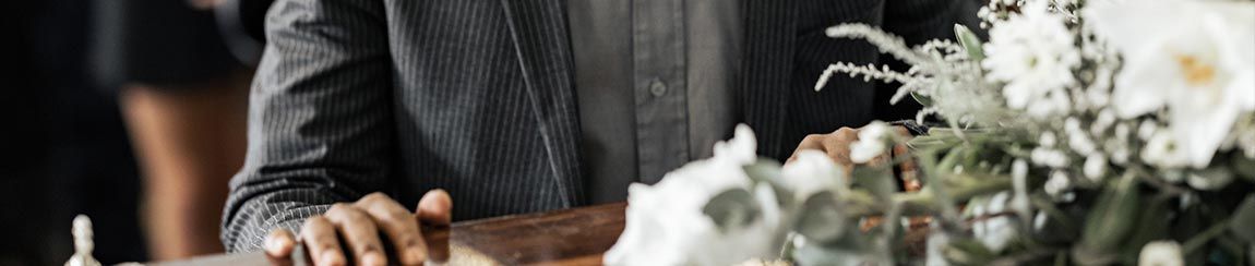 African American man stands solemnly beside white funeral flowers for a cremation