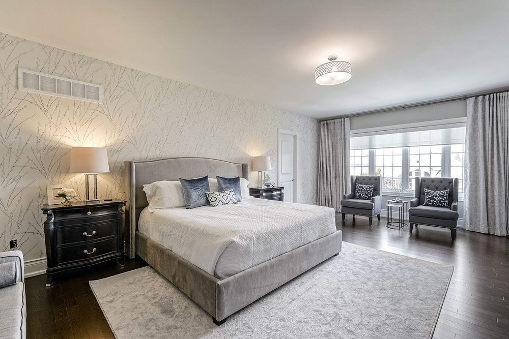 Bedroom with large bed, gray accents, patterned wallpaper, two armchairs, and a rug.