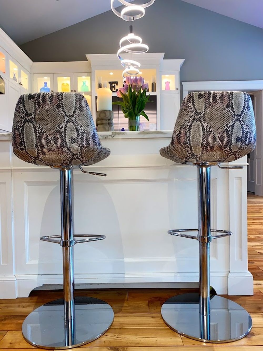 Two snakeskin-patterned bar stools in front of a white kitchen counter with a vase of pink flowers.