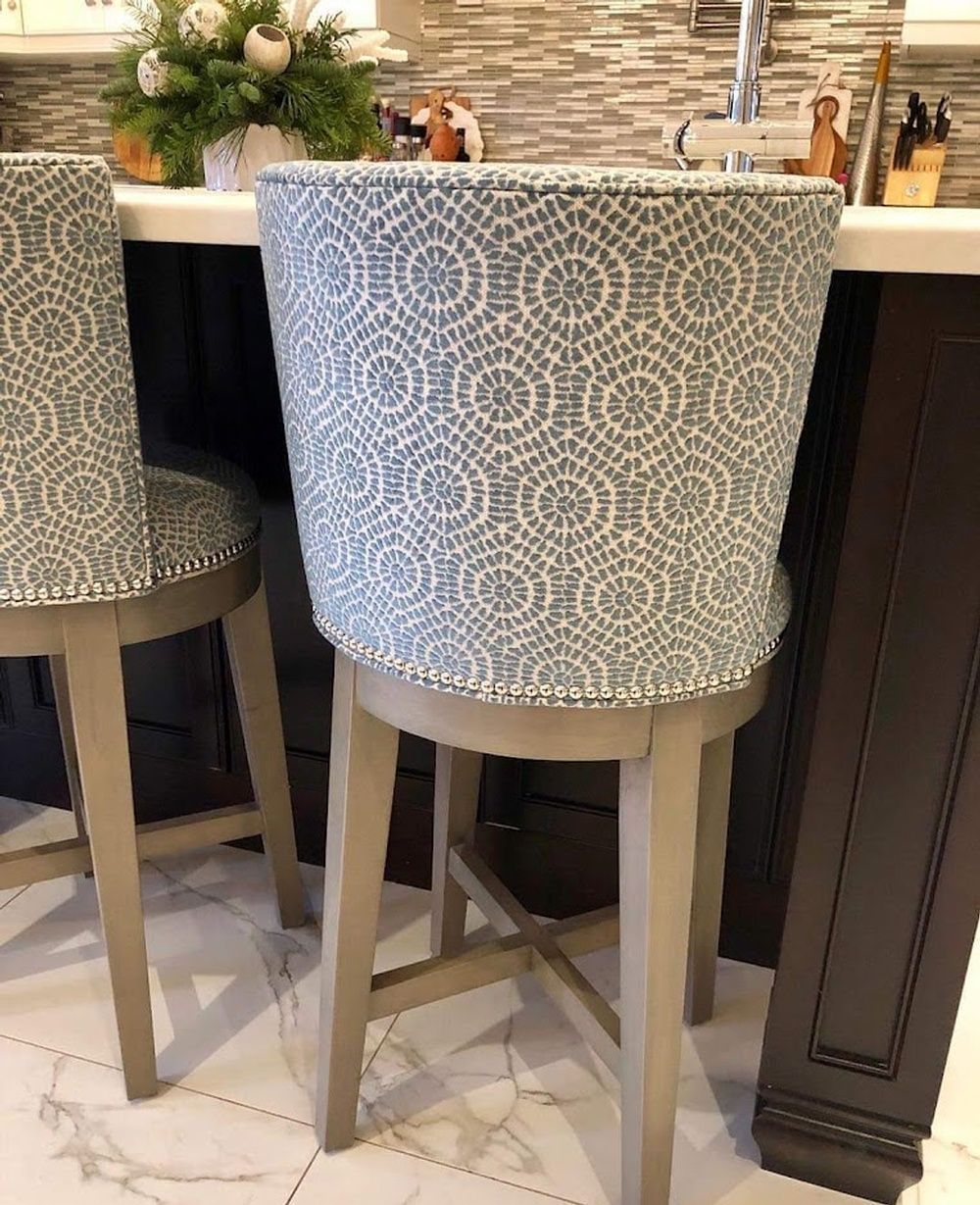 Two gray bar stools with blue and white patterned backs and seats, at a kitchen counter.
