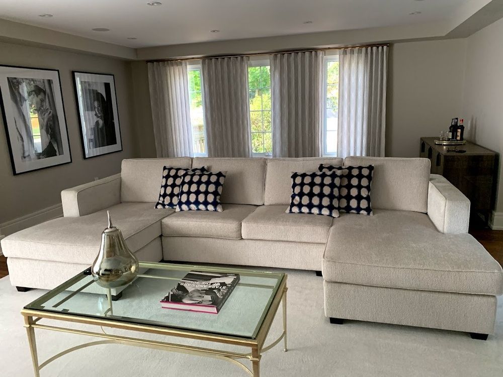 Beige sectional sofa in a living room, with art, curtains, and glass coffee table.