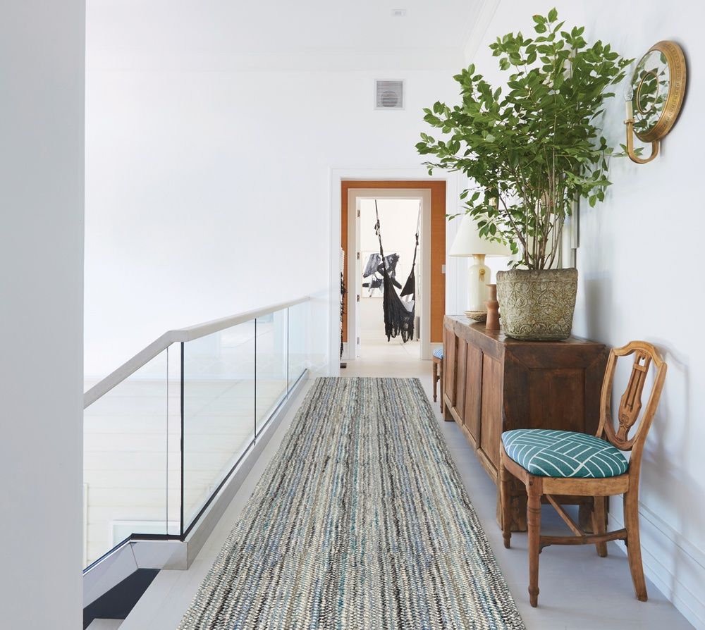 Hallway with a long rug, a wooden cabinet, greenery, and a chair.