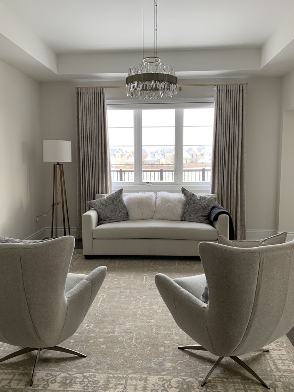Living room with sofa, two chairs, and a window with drapes; a chandelier hangs above.