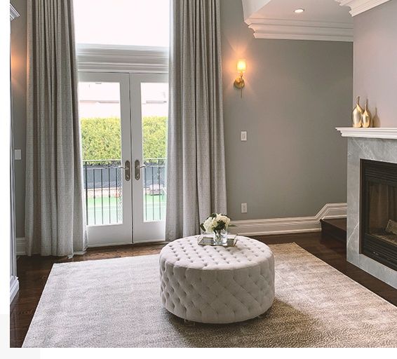 Living room with light gray walls, white trim, French doors, fireplace, and a tufted ottoman on a rug.