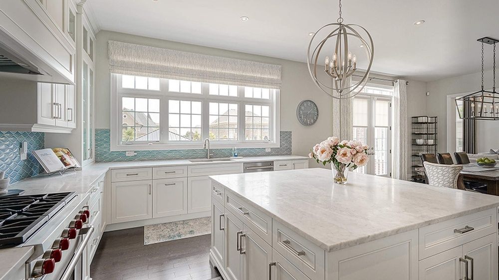 Bright white kitchen with large island, light blue backsplash, and chandelier.