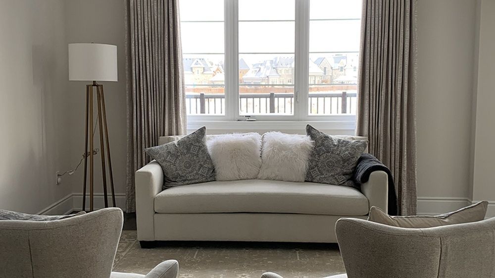 Living room with a beige sofa, patterned pillows, floor lamp, and window with curtains.