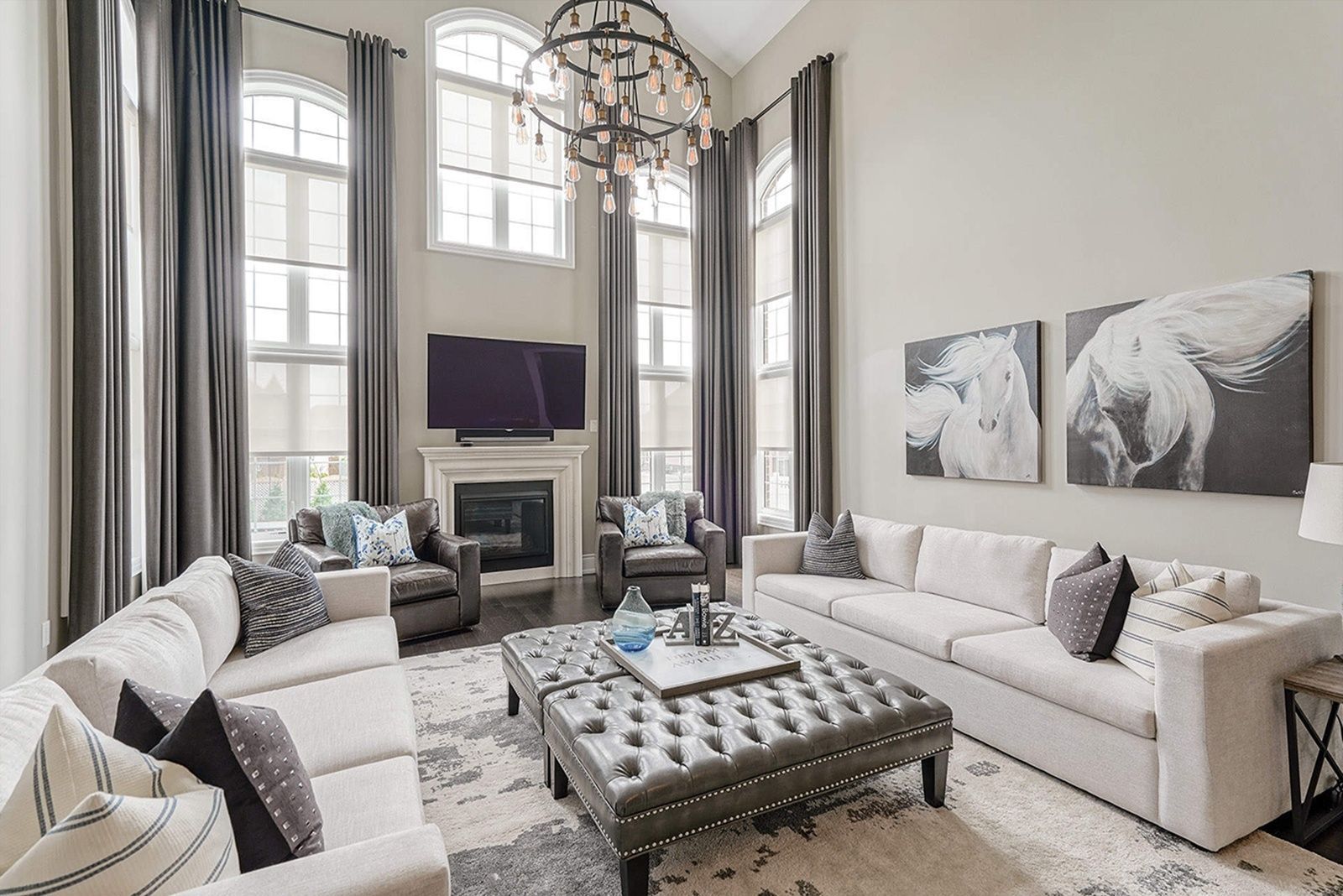 Living room with high ceilings, fireplace, large windows, and neutral-toned furniture; art on wall.