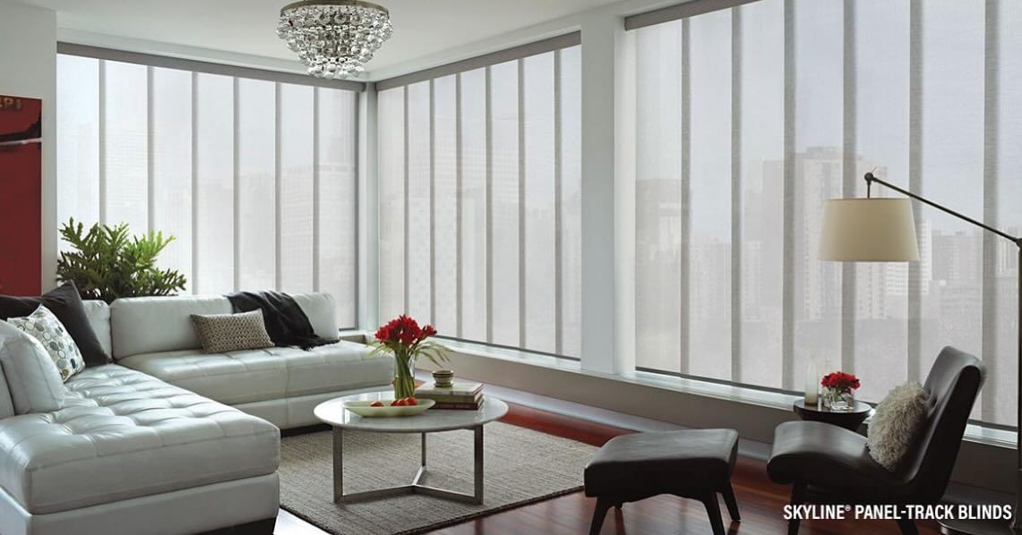 Modern living room with white couches, sheer blinds, and large windows.