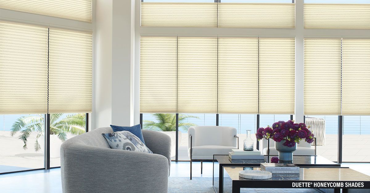 Living room with large windows, light yellow shades, gray seating, and ocean view.
