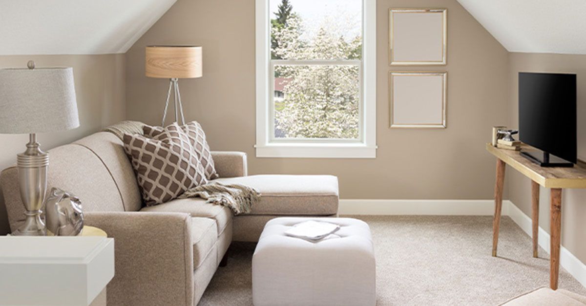 Cozy attic living space with a sectional sofa, ottoman, and television next to a window.