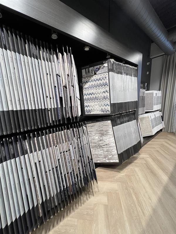 Display of gray and white tile samples in a store with wood flooring.