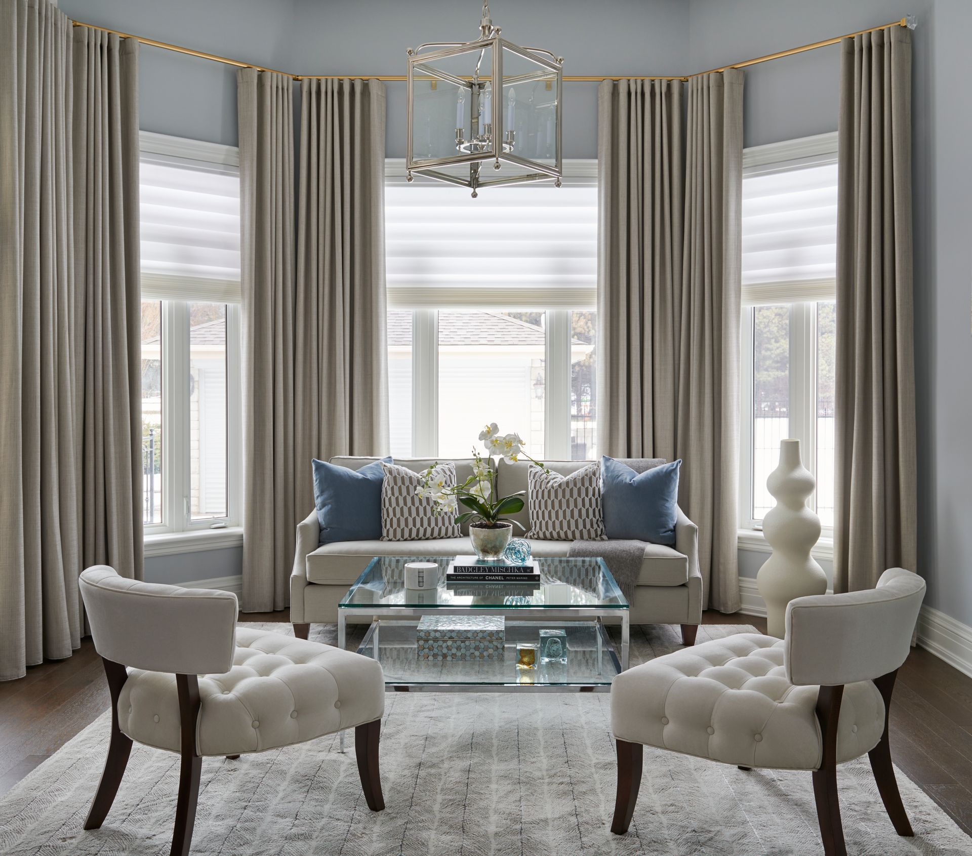 Living room with curved windows, curtains, sofa, chairs, and glass table.