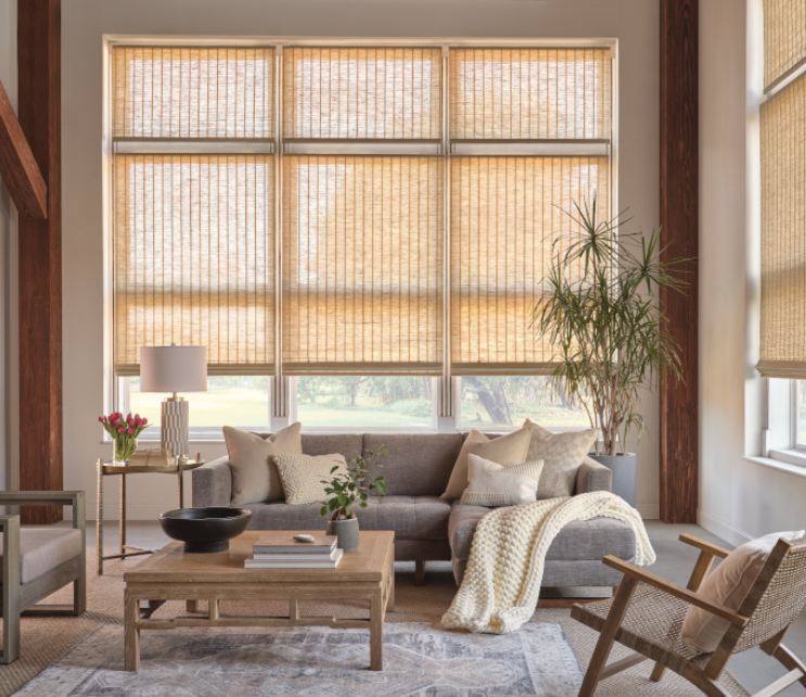 Living room with tall windows covered with beige shades, gray sectional sofa, and wood furniture.